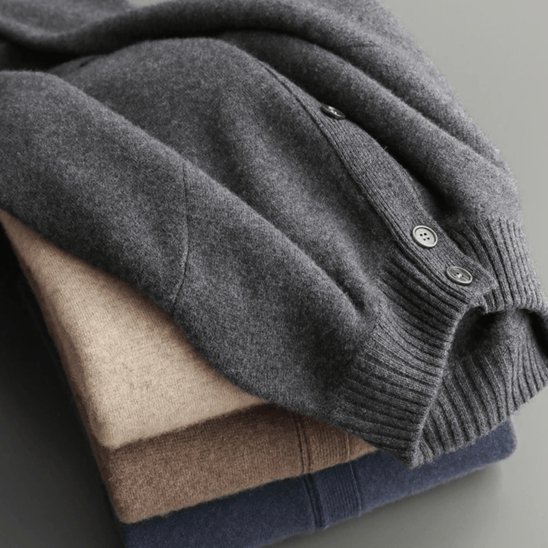 Stack of folded sweaters in gray, beige, and navy on a light gray background