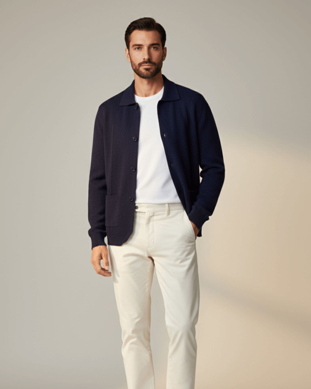 Man wearing a navy cardigan, white shirt, and light-colored pants against a neutral background
