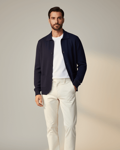 Man wearing a navy cardigan, white shirt, and light-colored pants against a neutral background