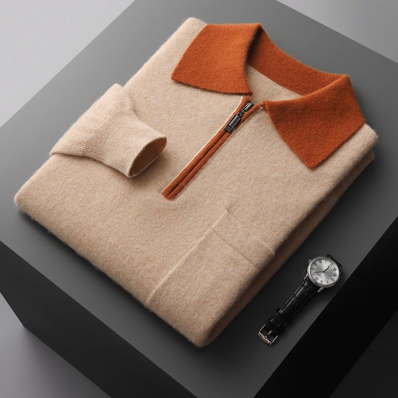 Folded beige sweater with orange collar on a dark surface, next to a watch.