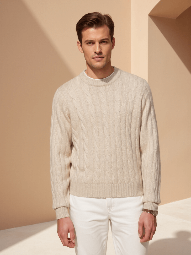 Man wearing a beige cable knit sweater and white pants against a beige background