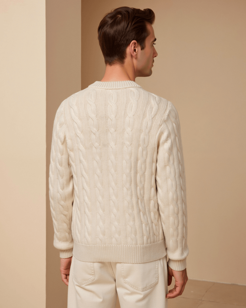 Man wearing a cream cable knit sweater and pants against a beige wall.