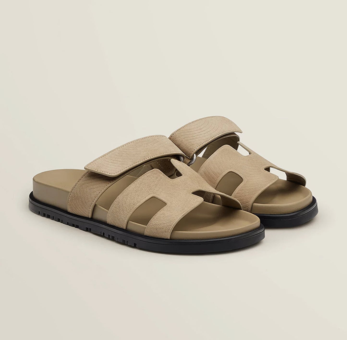 Pair of beige sandals with black soles on a light beige background
