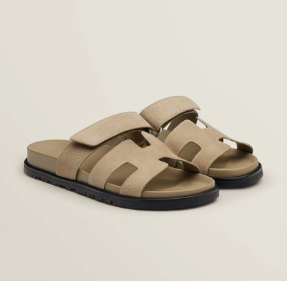 Pair of beige sandals with black soles on a light beige background