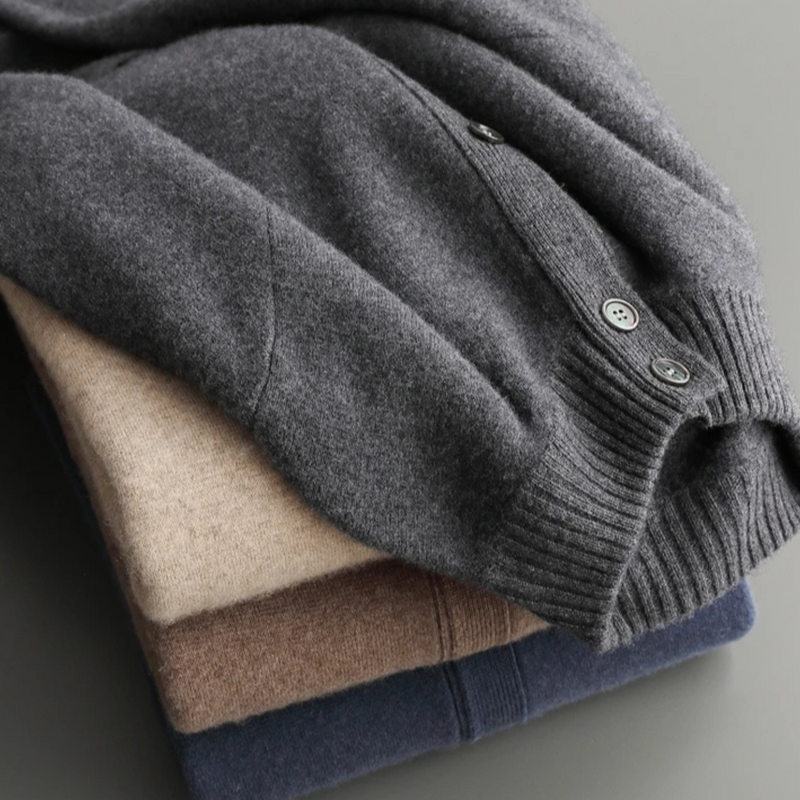 Stack of folded sweaters in various colors on a neutral background
