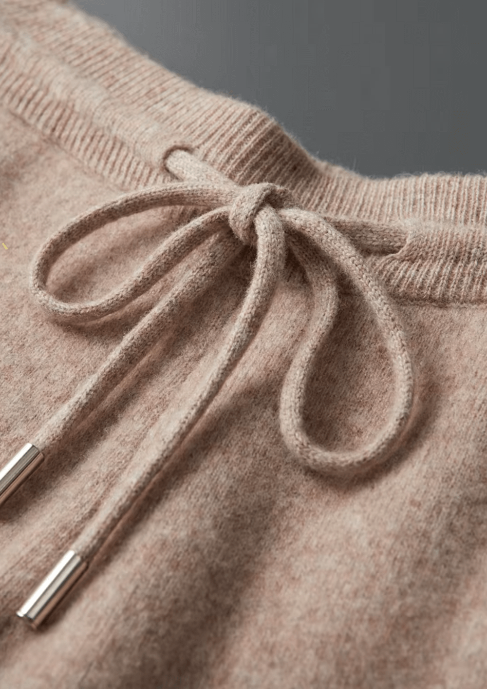 Close-up of a beige knitted sweater with a drawstring detail.