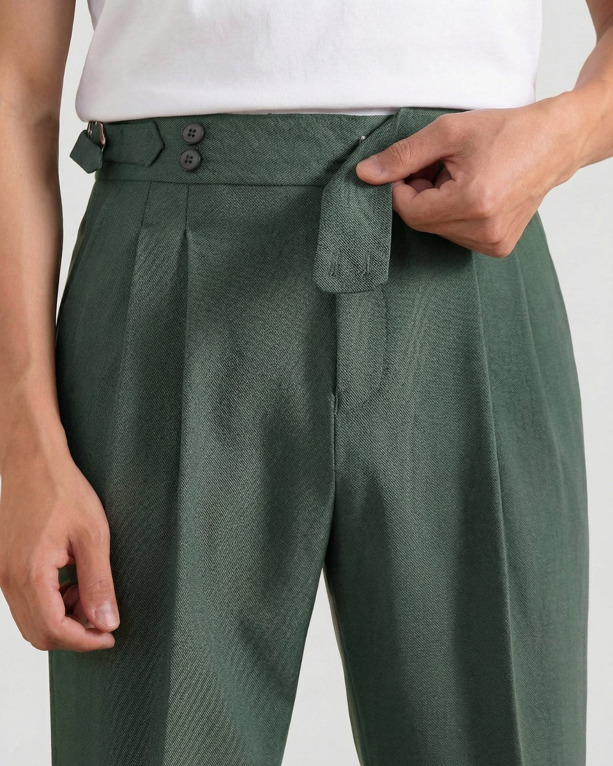 Close-up of forest green double-pleated cotton blend trousers showing extended crossover button waistband and side buckle