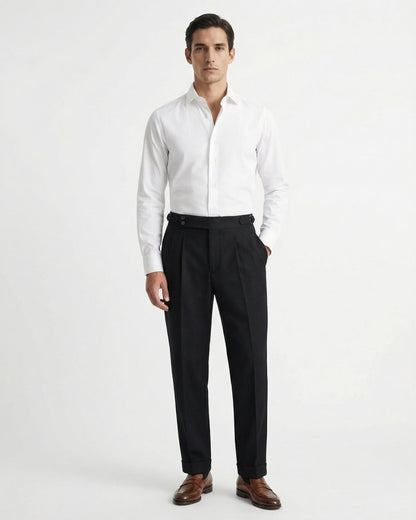 Men's black double-pleated cotton blend trousers showing extended crossover button waistband and side buckle