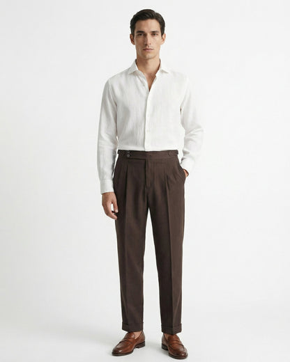 Men's brown double-pleated cotton blend trousers showing extended crossover button waistband and side buckle