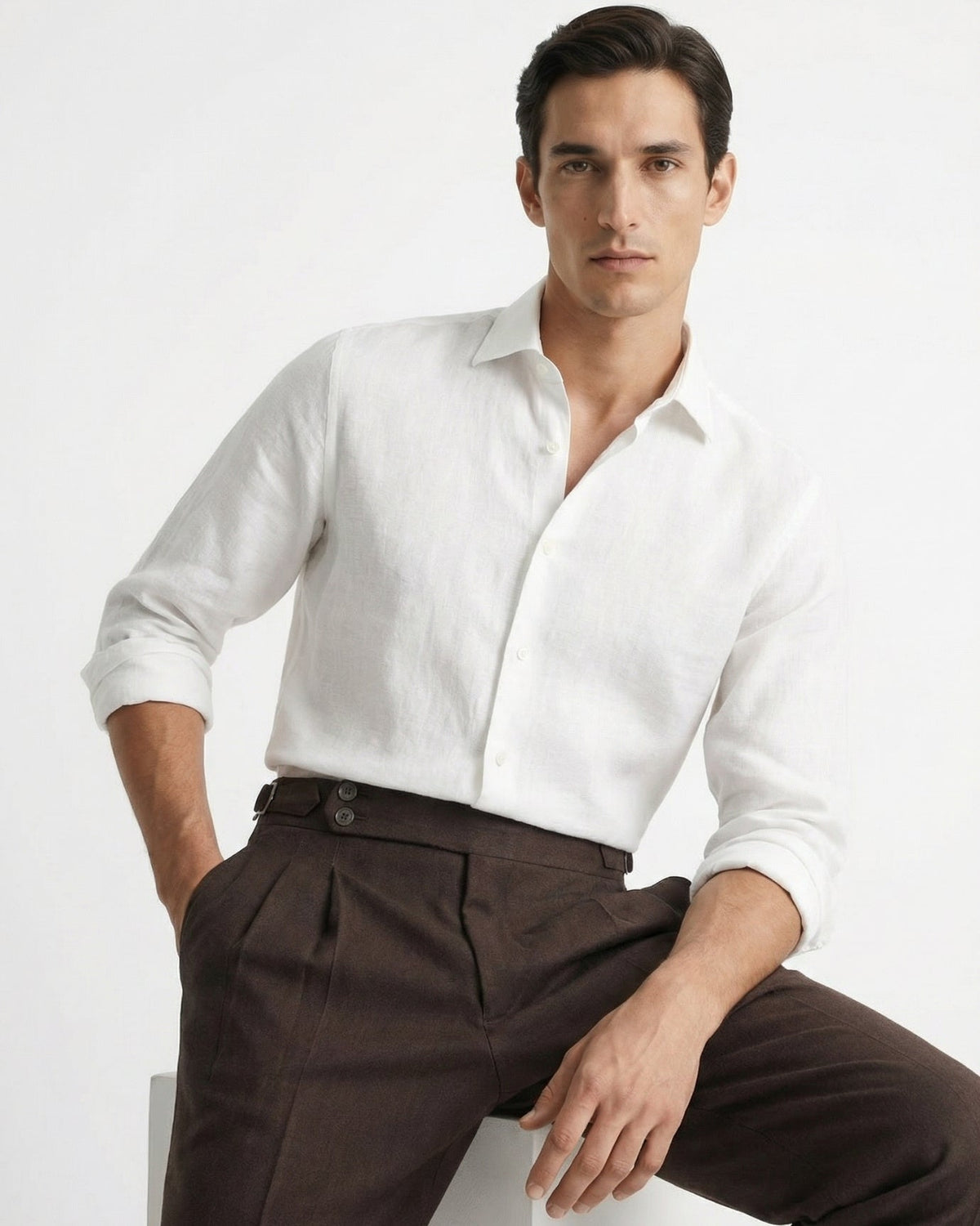 Men's brown double-pleated cotton blend trousers showing extended crossover button waistband and side buckle