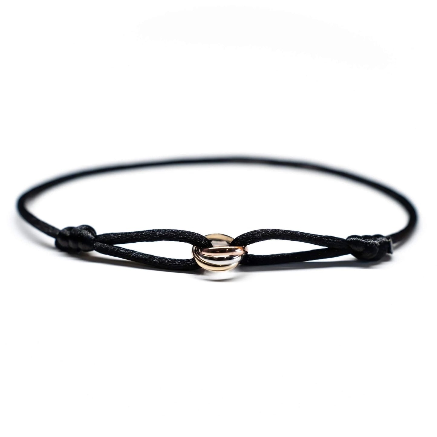 Black cord bracelet with gold and silver circular charms on a white background
