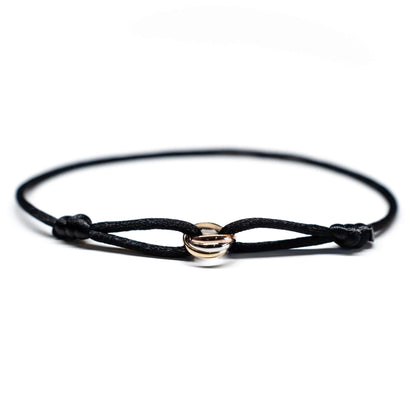 Black cord bracelet with gold and silver circular charms on a white background