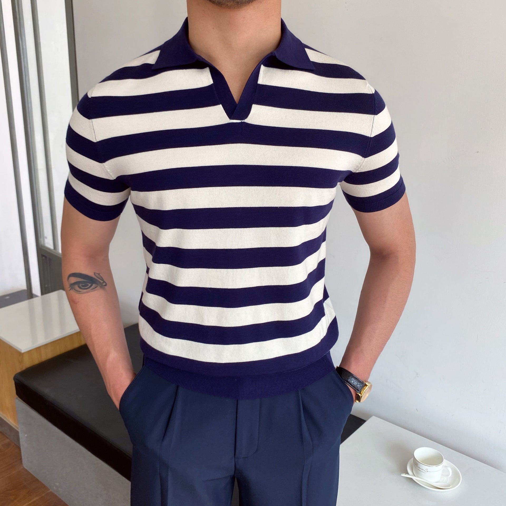 Person wearing a navy and white striped polo shirt with blue pants indoors.