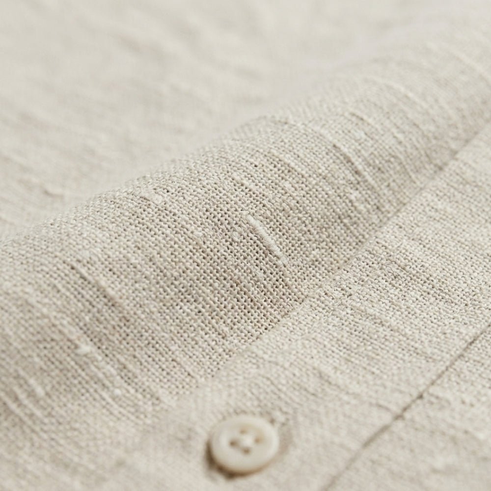 Men's beige short sleeve linen shirt featuring a natural slub texture, chest pocket, and a relaxed tailored fit.