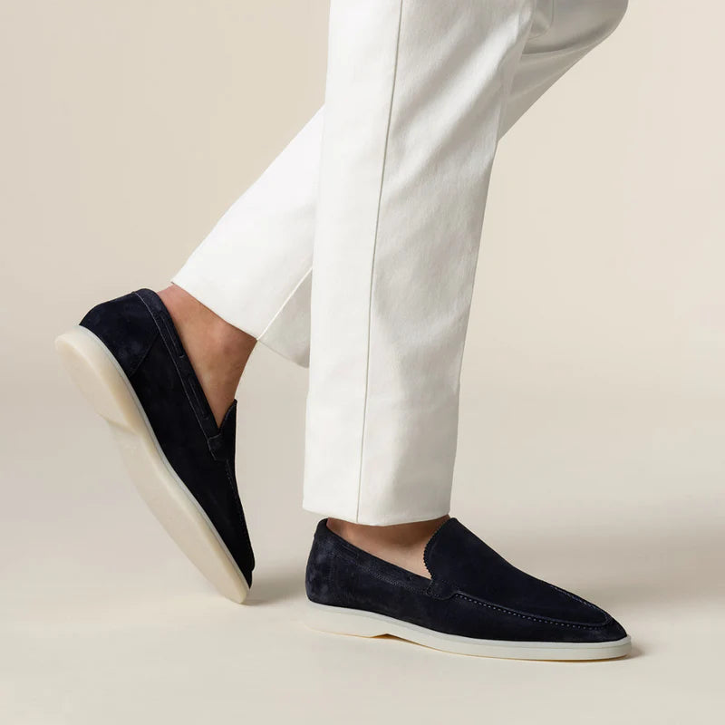 Navy loafers worn with white pants on a beige background
