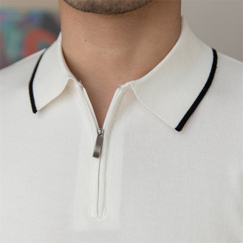Close-up of a white high-gauge knit polo featuring a black tipped collar and a sleek metallic quarter-zip placket.