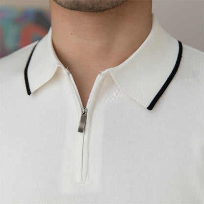 Close-up of a white high-gauge knit polo featuring a black tipped collar and a sleek metallic quarter-zip placket.