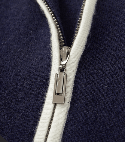 Close-up of the silver-tone metal zipper and white contrast piping on the navy merino wool polo cardigan.