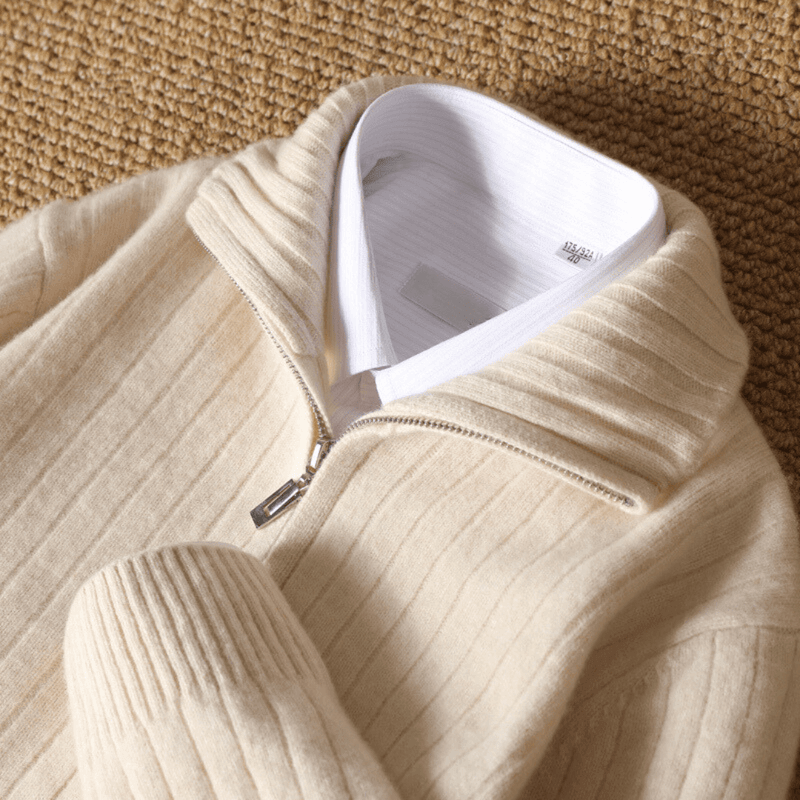 Beige ribbed sweater with a white shirt underneath on a textured surface