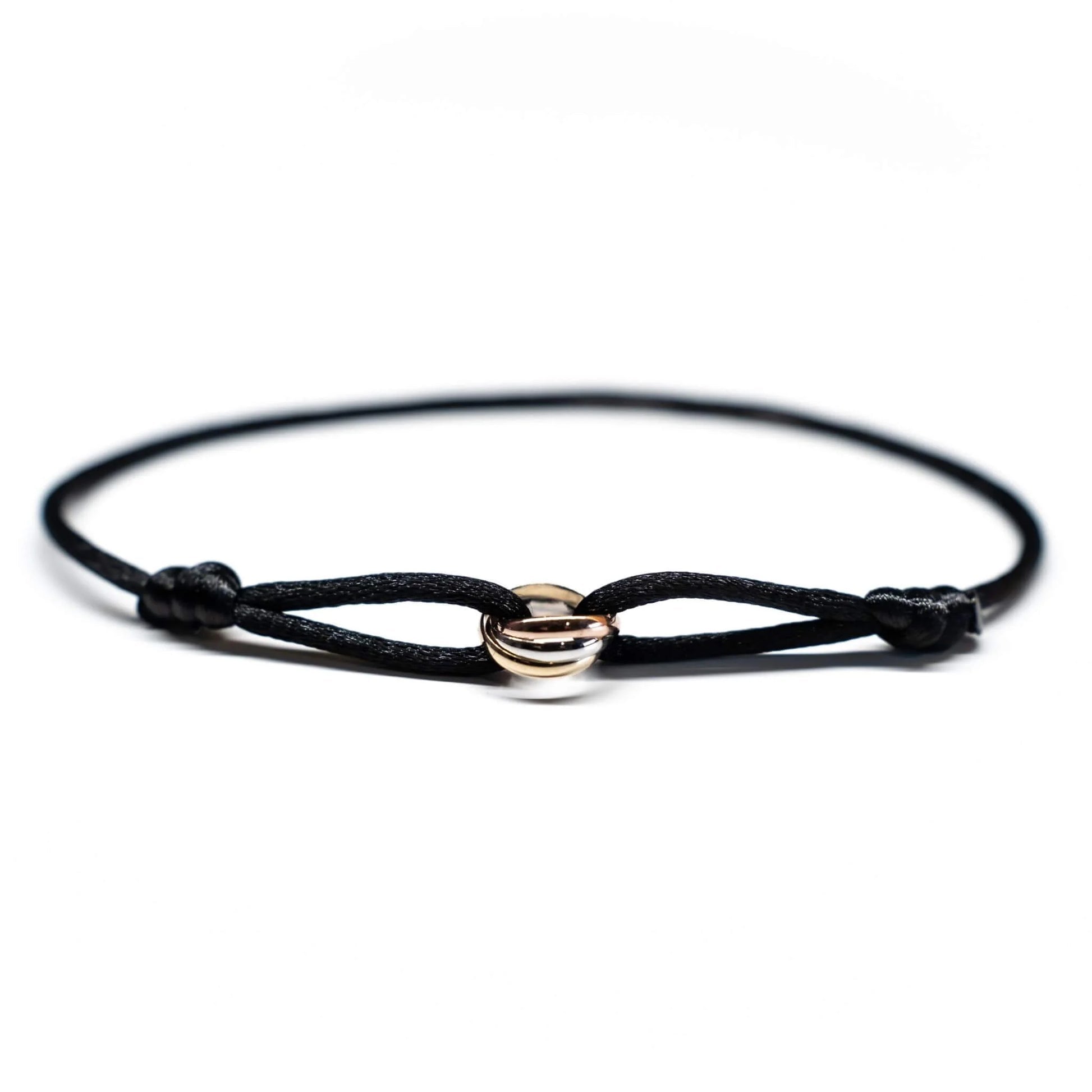 Black cord bracelet with gold and silver circular charms on a white background