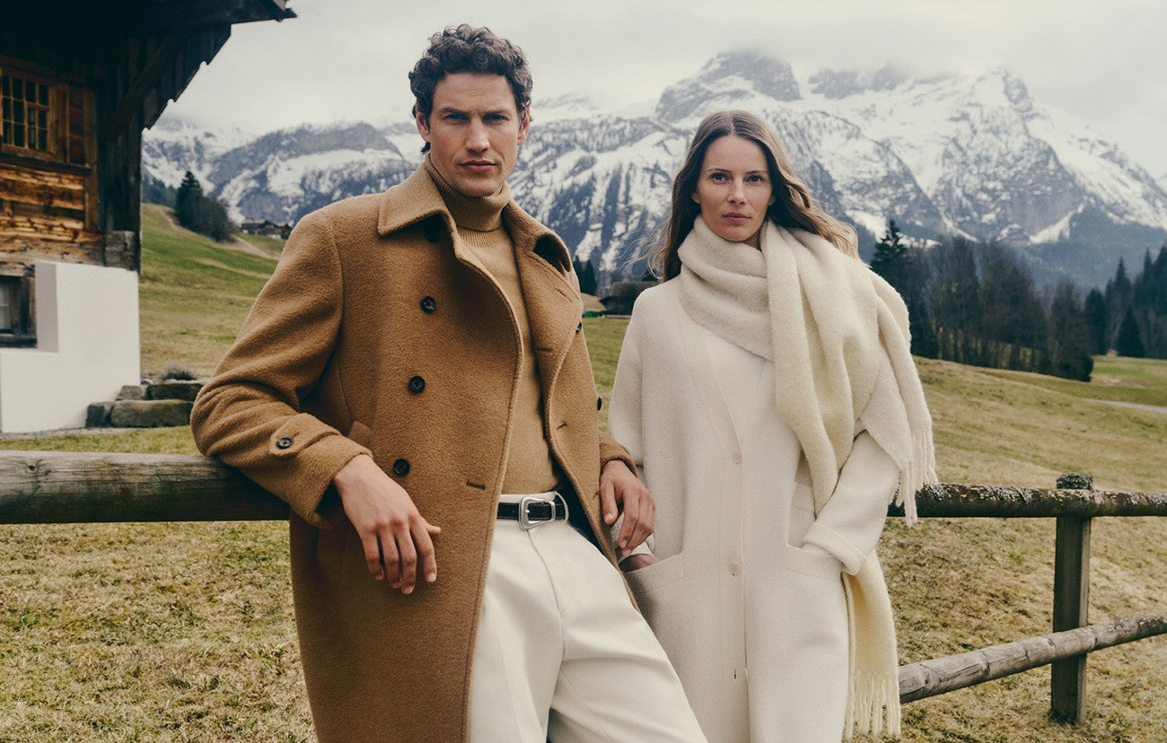 Two people standing in a snowy mountain landscape with a wooden cabin.