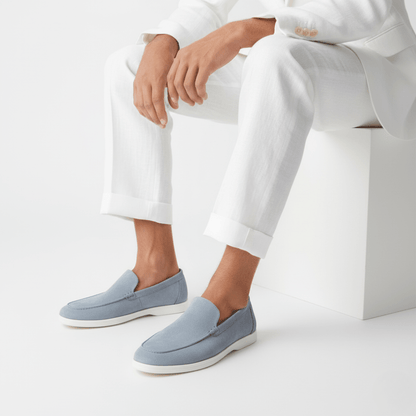 Person wearing a light blue premium suede loafers featuring a classic apron toe and a lightweight off-white rubber sole.