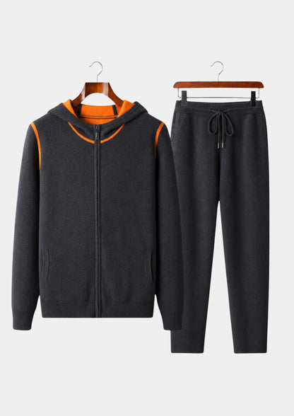 Men's dark grey 100% cashmere set featuring a full-zip hoodie with silver hardware and matching tapered knit pants with a drawstring waist.