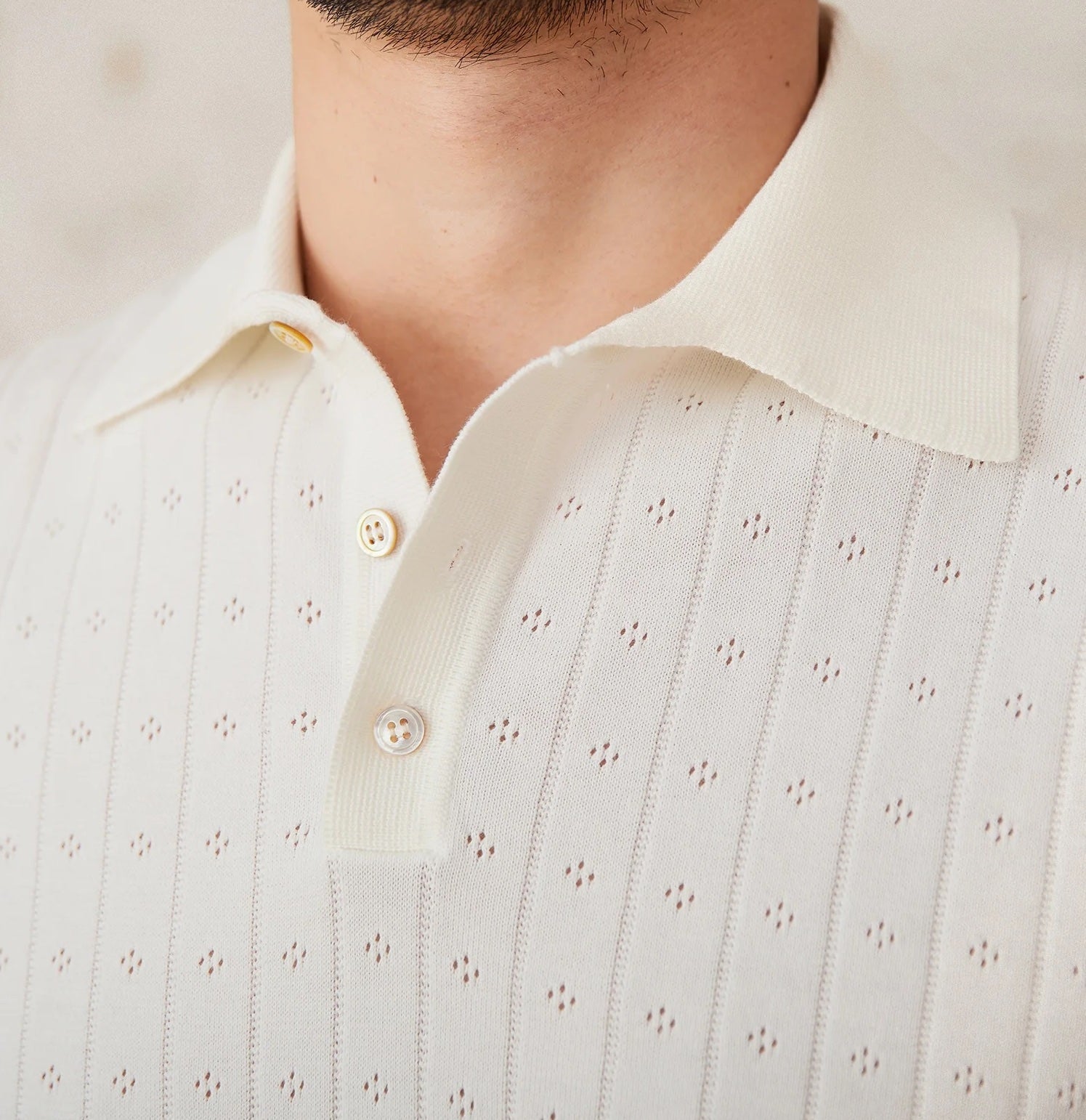 Men's crisp white 100% cotton polo featuring an intricate pointelle vertical ribbed texture and a refined buttoned placket.