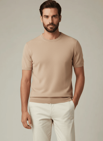 Man wearing a beige pure cashmere crewneck t-shirt and white pants against a plain background