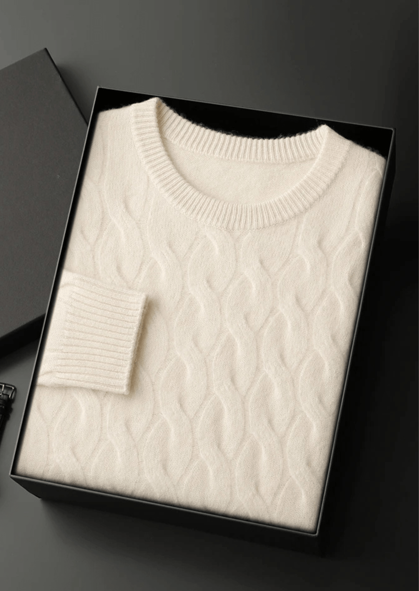 White cable knit sweater in a black box on a dark background