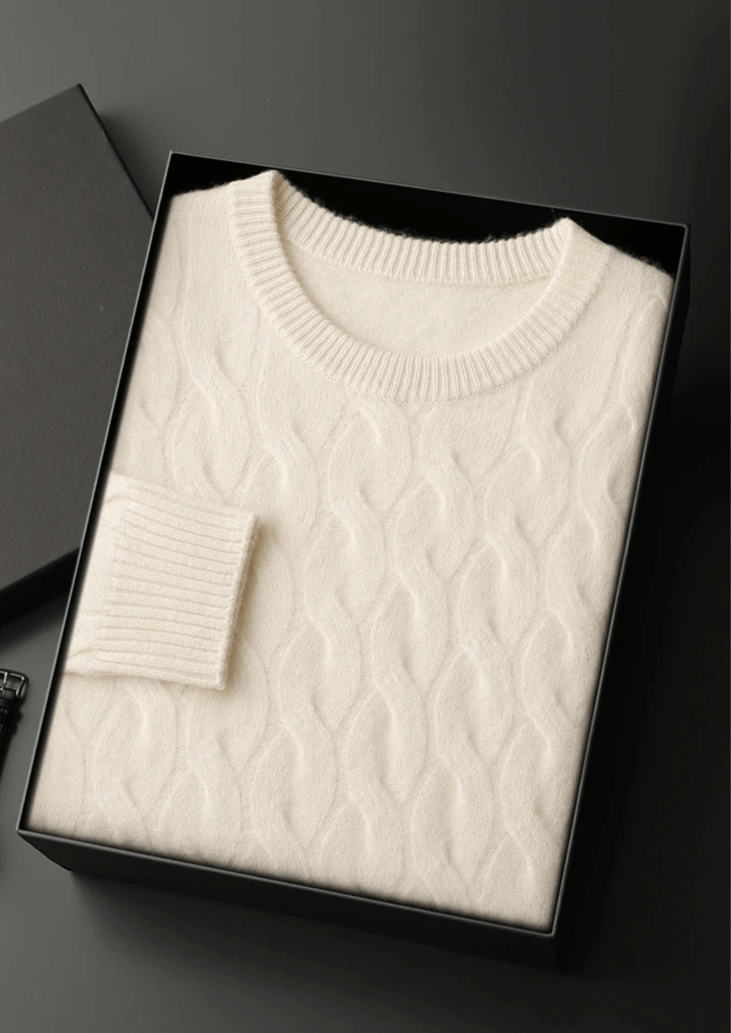 White cable knit sweater in a black box on a dark background