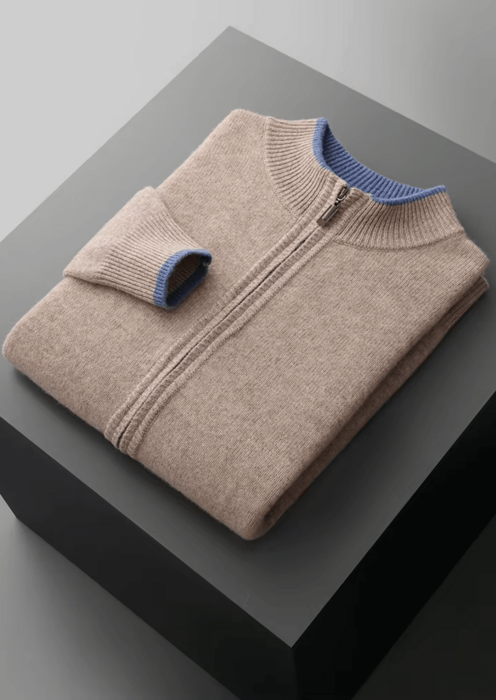 Folded beige sweater with blue trim on a gray surface