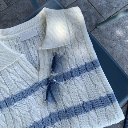 Close-up of a cream-colored silk and linen cable knit polo shirt with light blue horizontal stripes and a V-neck open collar, featuring clear frame sunglasses tucked into the neckline.