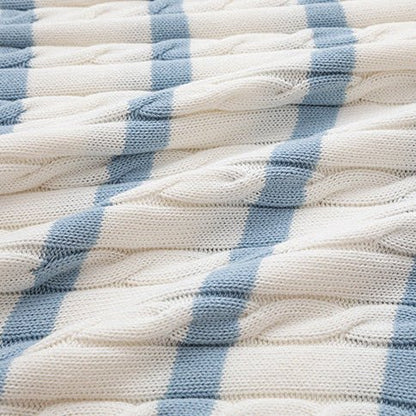 Close-up of a cream-colored silk and linen cable knit polo shirt with light blue horizontal stripes and a V-neck open collar, featuring clear frame sunglasses tucked into the neckline.