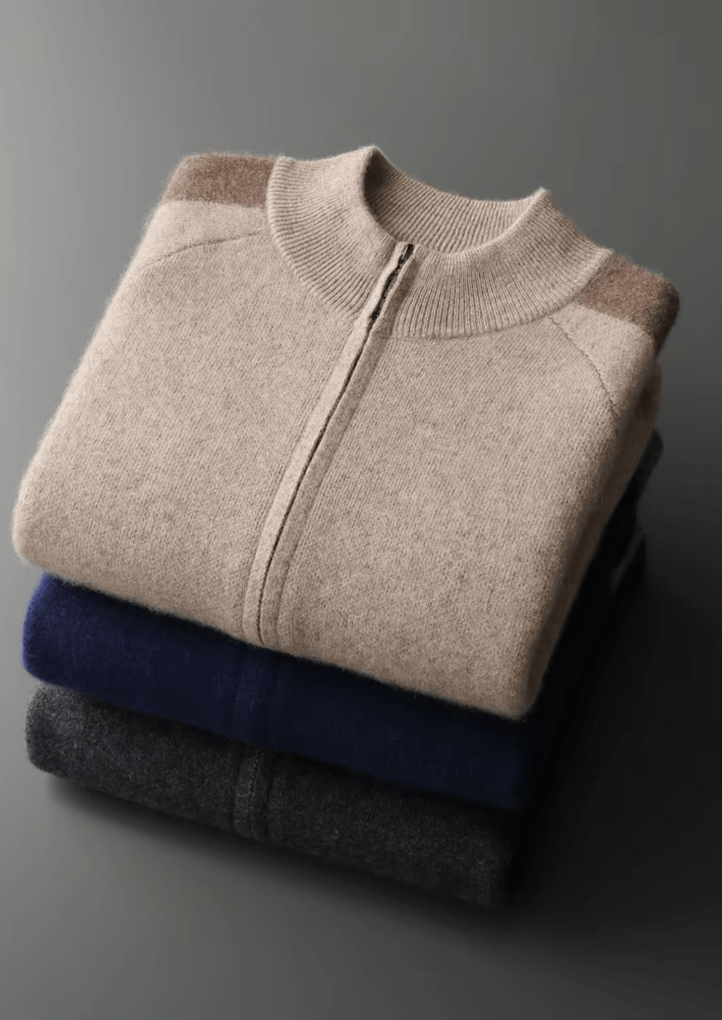 Stack of folded sweaters in beige, blue, and gray on a dark background