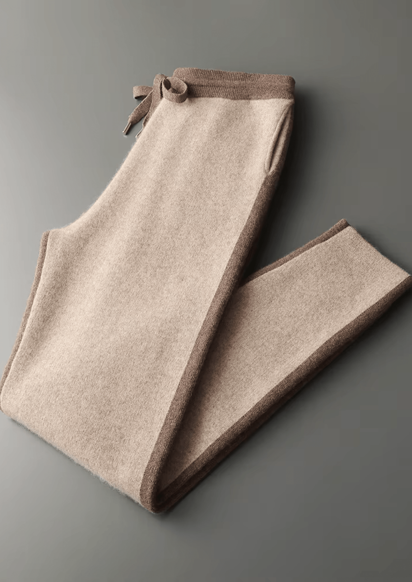 Folded beige pants with brown trim on a gray background