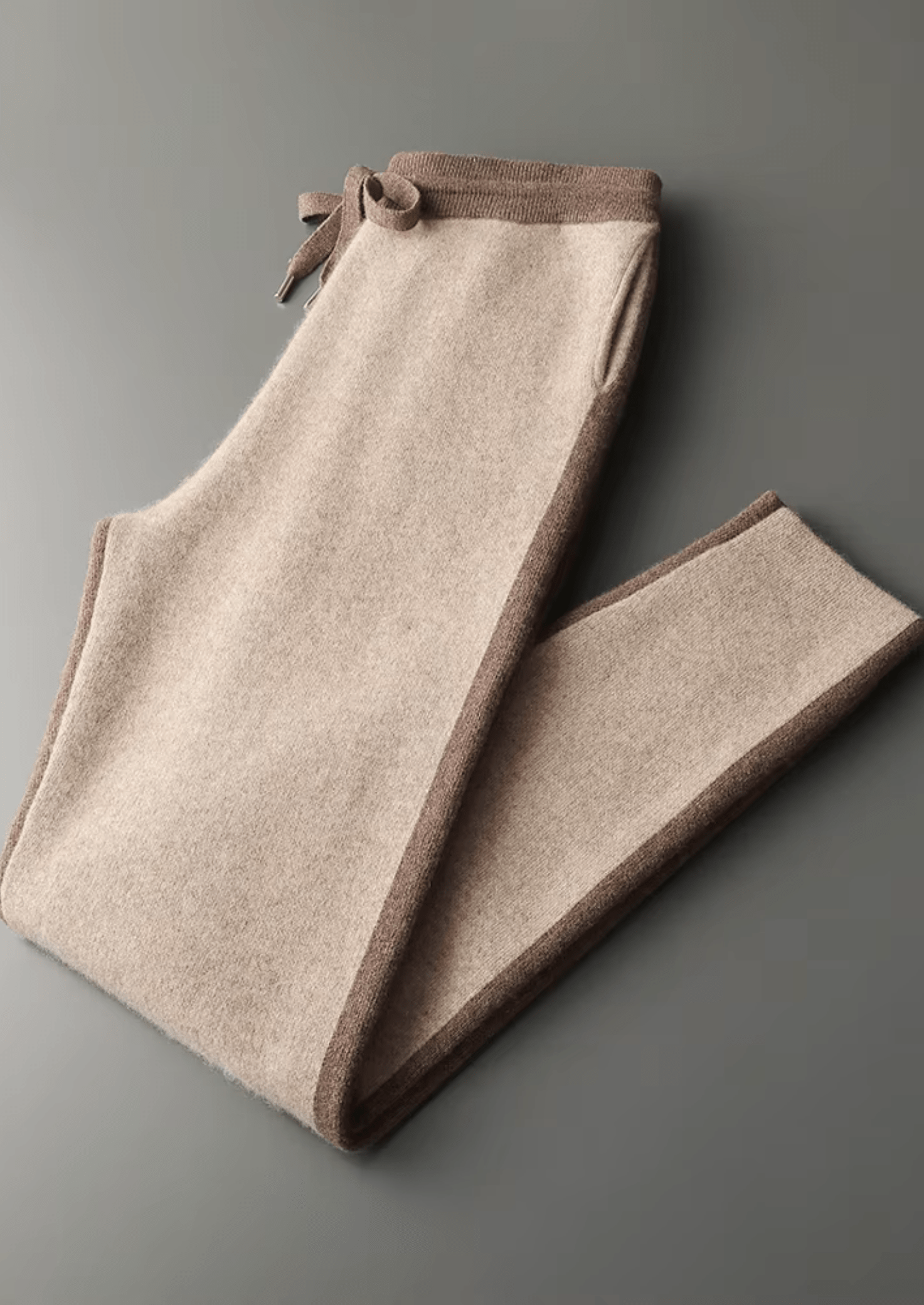 Folded beige pants with brown trim on a gray background