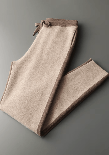 Folded beige pants with brown trim on a gray background