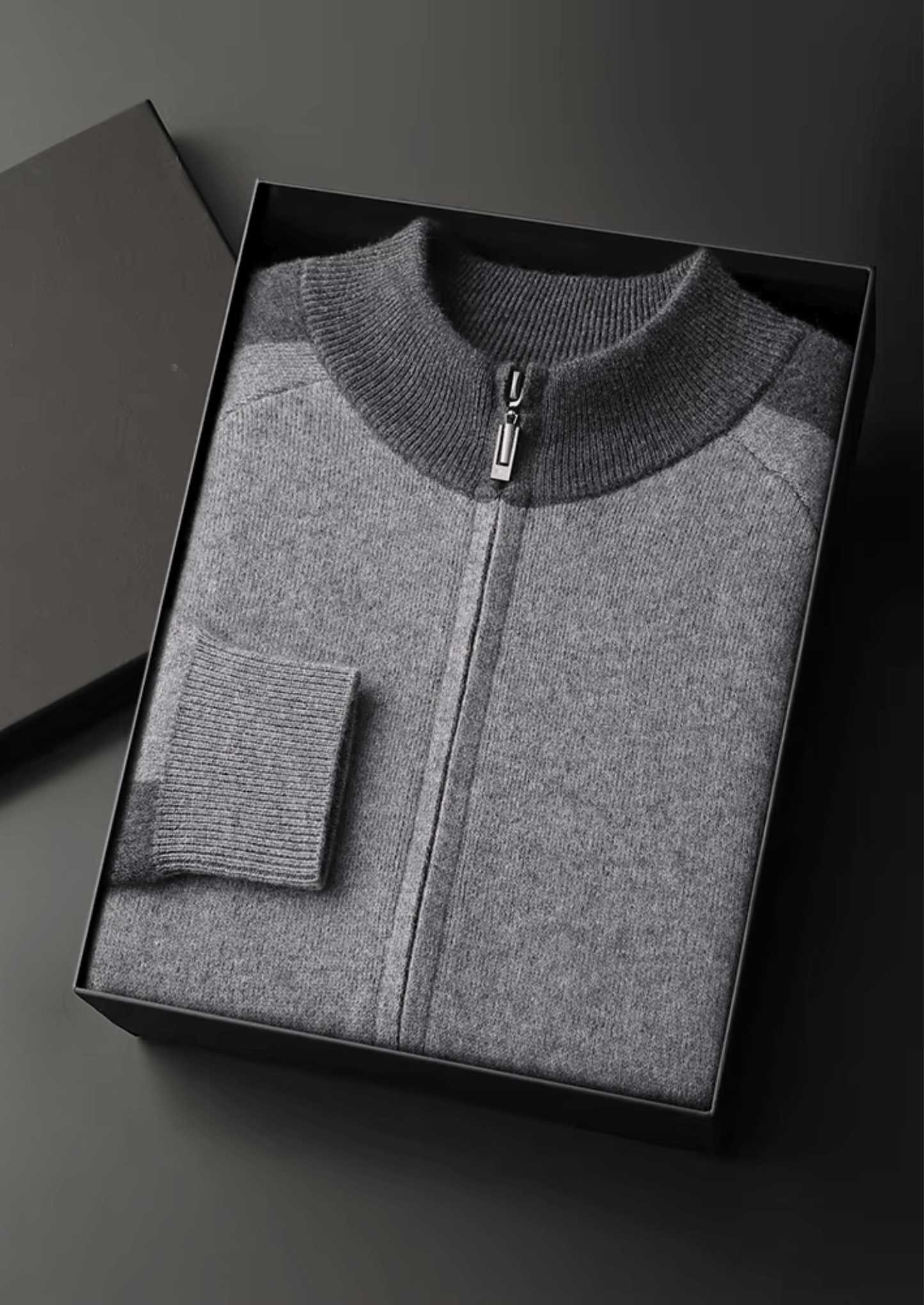 Gray zip-up sweater in a black box on a dark background