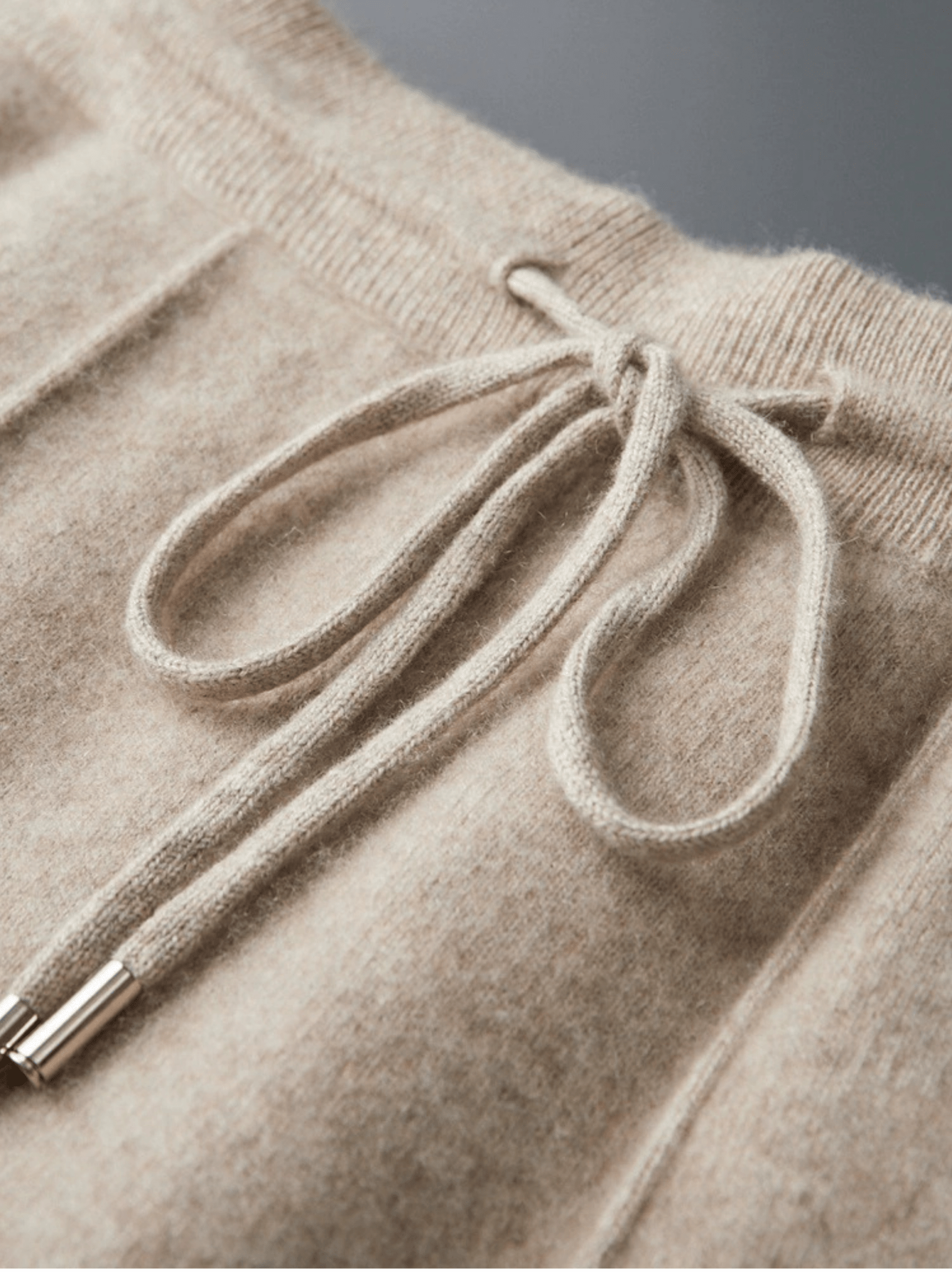 Close-up of a beige knitted sweater with a drawstring detail on a gray background