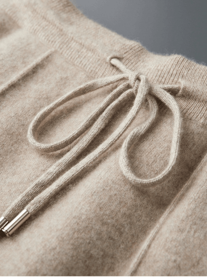 Close-up of a beige knitted sweater with a drawstring detail on a gray background