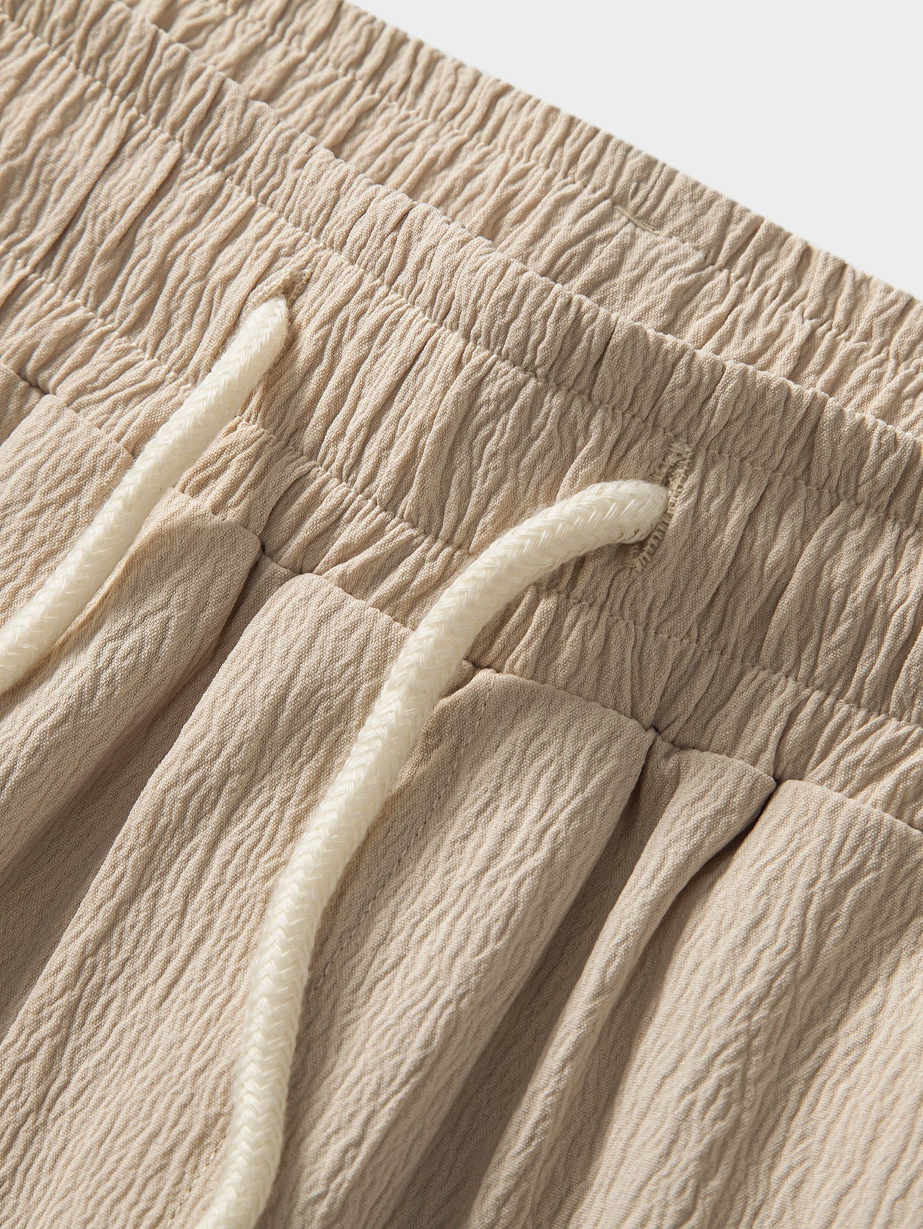 Close-up of beige textured fabric with a white cord detail.